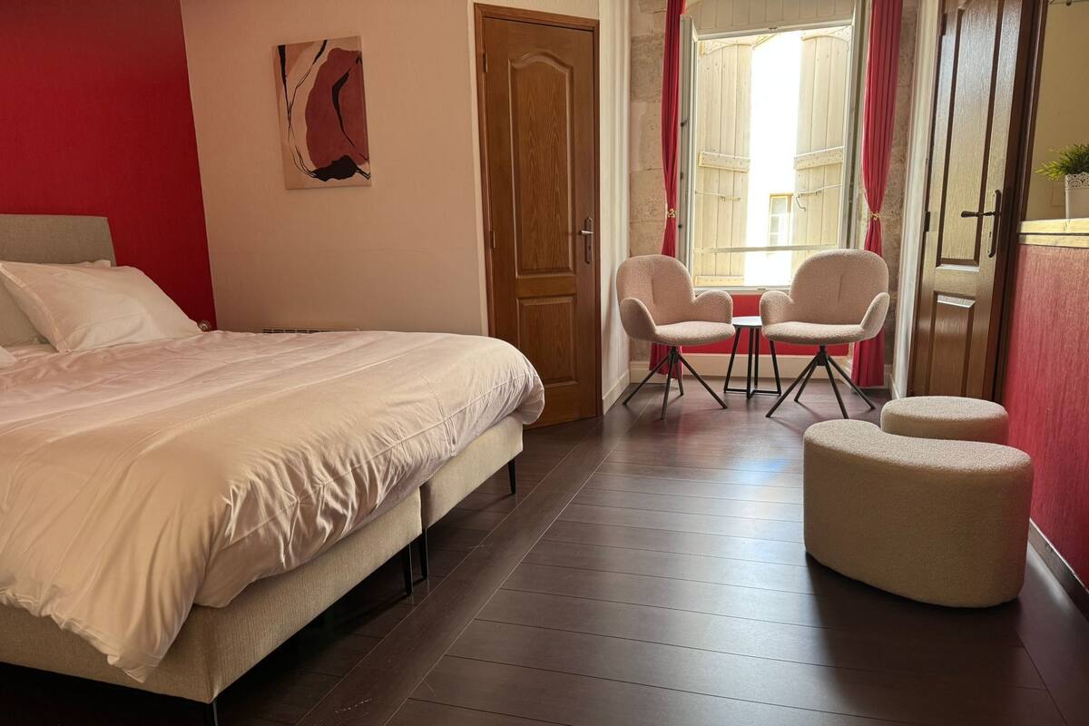 Un dormitorio con cama, una silla, una mesita y una ventana con cortinas.