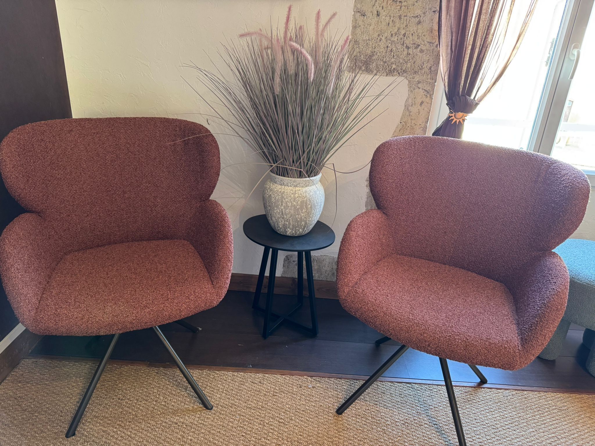 Two matching armchairs with a textured fabric, a small round table with a decorative vase, and a tall plant beside them.
