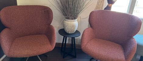 Two matching armchairs with a textured fabric, a small round table with a decorative vase, and a tall plant beside them.