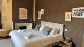 Un dormitorio de hotel con una cama grande, una chimenea de mármol y obras de arte enmarcadas en las paredes.