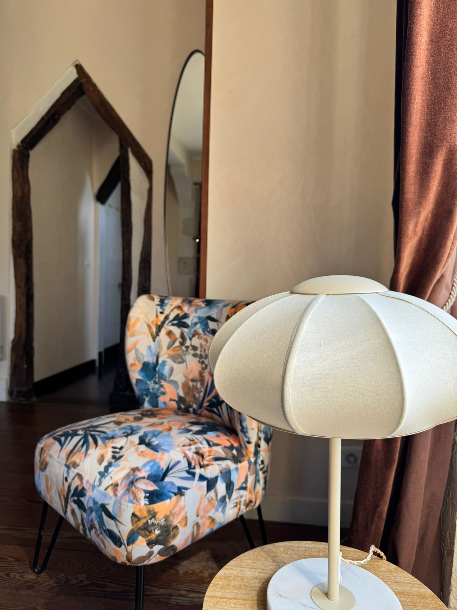 Una habitación con una silla de estampado floral, una mesa redonda de madera y una lámpara de pie.