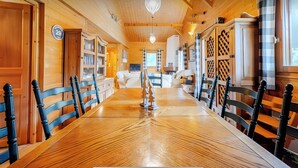 Ein Holzinterieur mit einem langen Esstisch, Stühlen, einer Chandelüstere und Blick ins Freie.