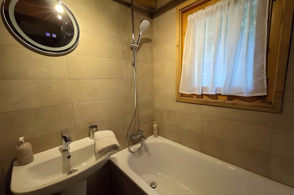 A bathroom with a sink, mirror, shower, and window with curtains.