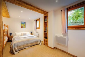 Een slaapkamer met een bed, een houten hoofdbord, een raam met gordijnen, een radiator en een plank met boeken.