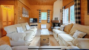 Ein gemütliches Blockhaus-Interieur mit Holzwänden, zwei Sofas, einem Fernseher und einem Kamin.