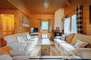 Een gezellig chaletinterieur met houten wanden, twee banken, een televisie en een open haard.