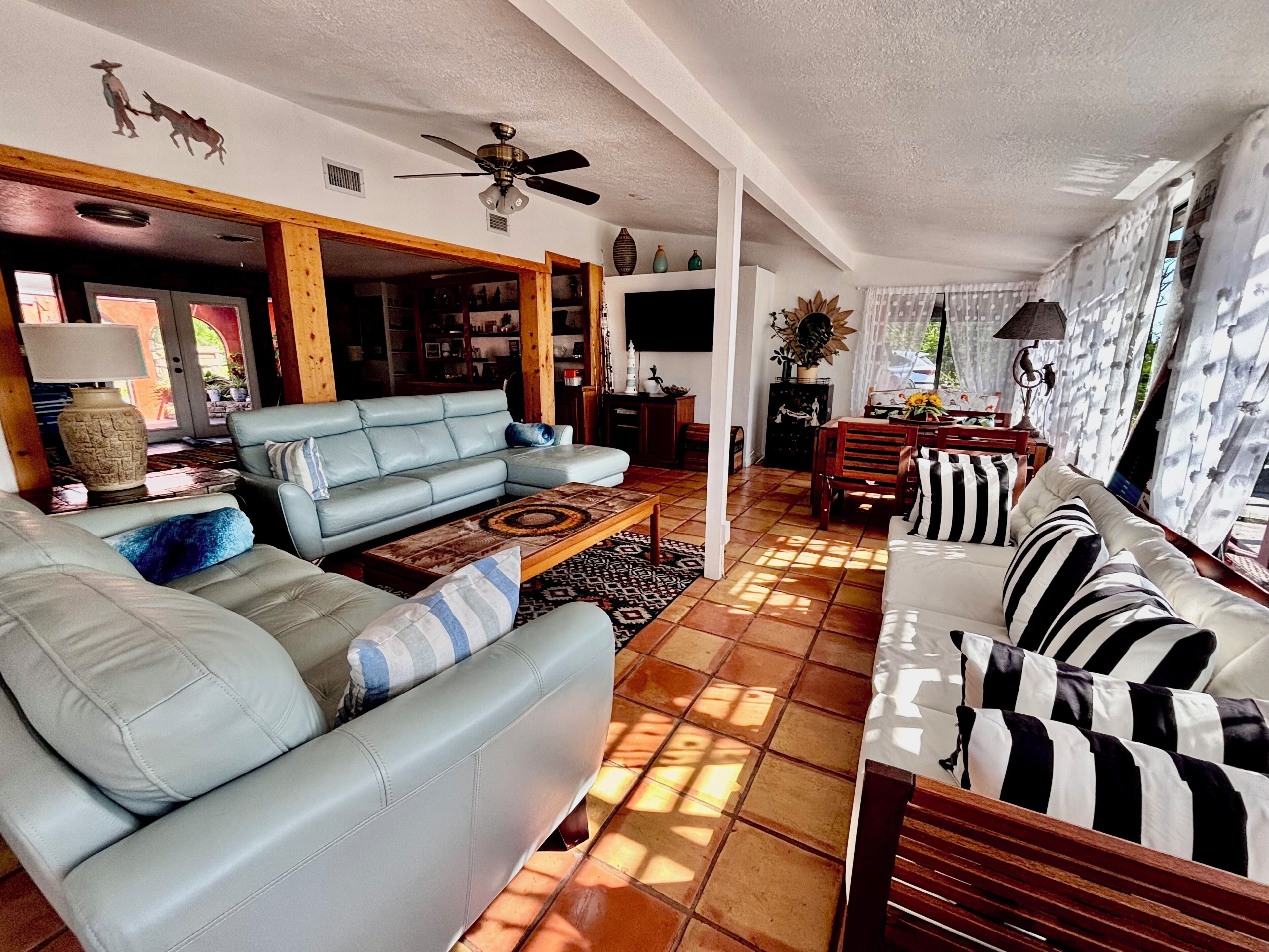 A spacious living room with a light blue sofa, a wooden coffee table, and a dining area with a striped sofa.