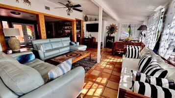 A spacious living room with a light blue sofa, a wooden coffee table, and a dining area with a striped sofa.