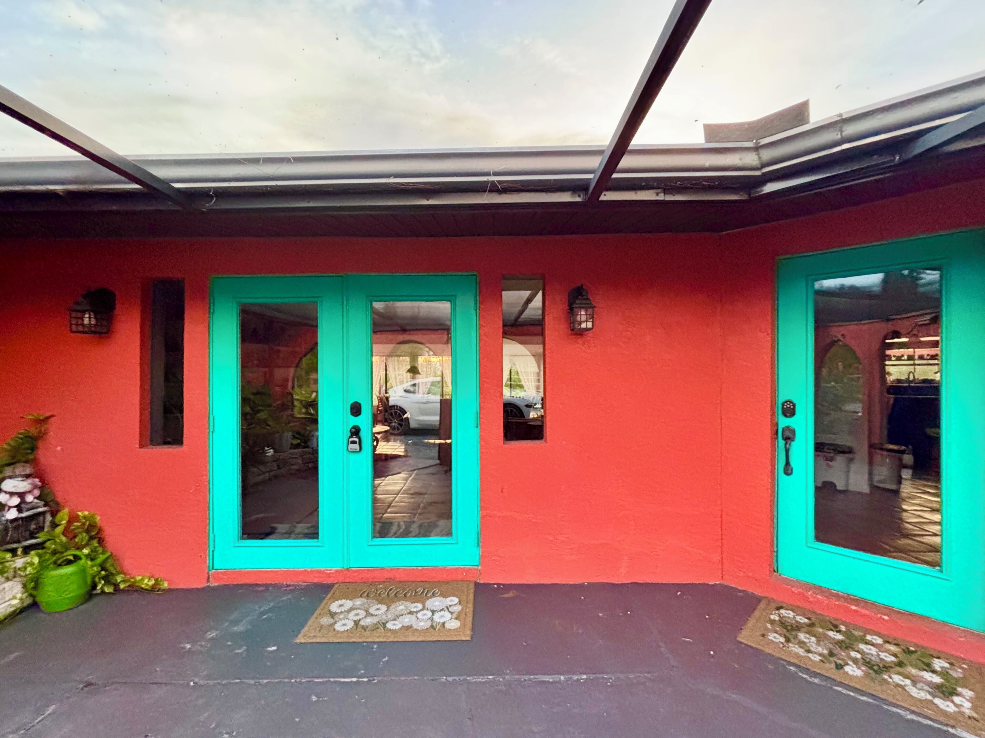 A red building with turquoise doors and windows, a doormat with a welcome message, and a clear sky above.