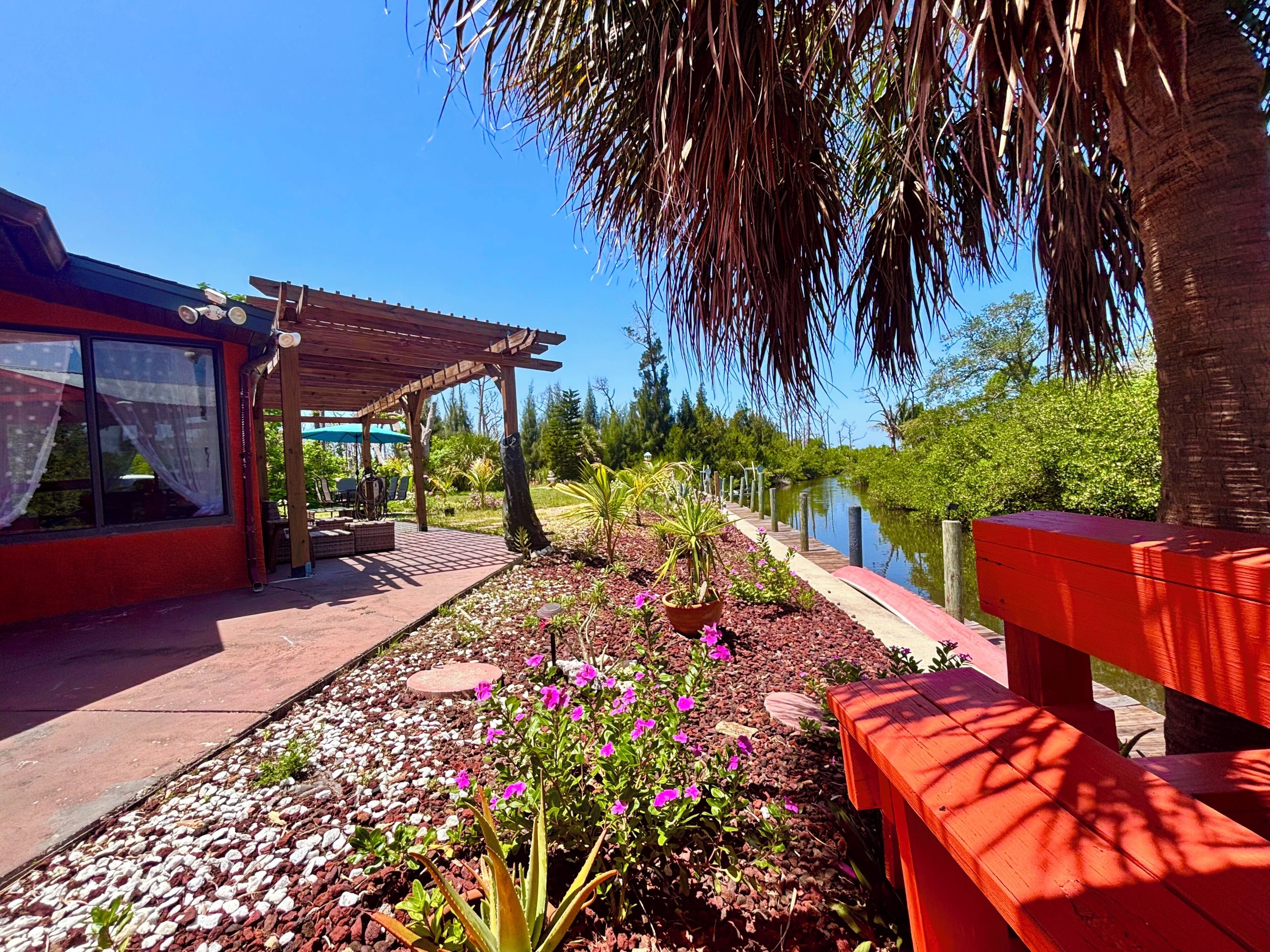 Zona de pati amb una pèrgola de fusta, seients exteriors i un jardí amb flors i plantes.