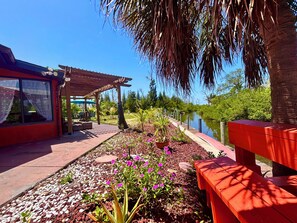 Una zona patio con una pergola in legno, posti a sedere all'aperto e un giardino con fiori e piante.