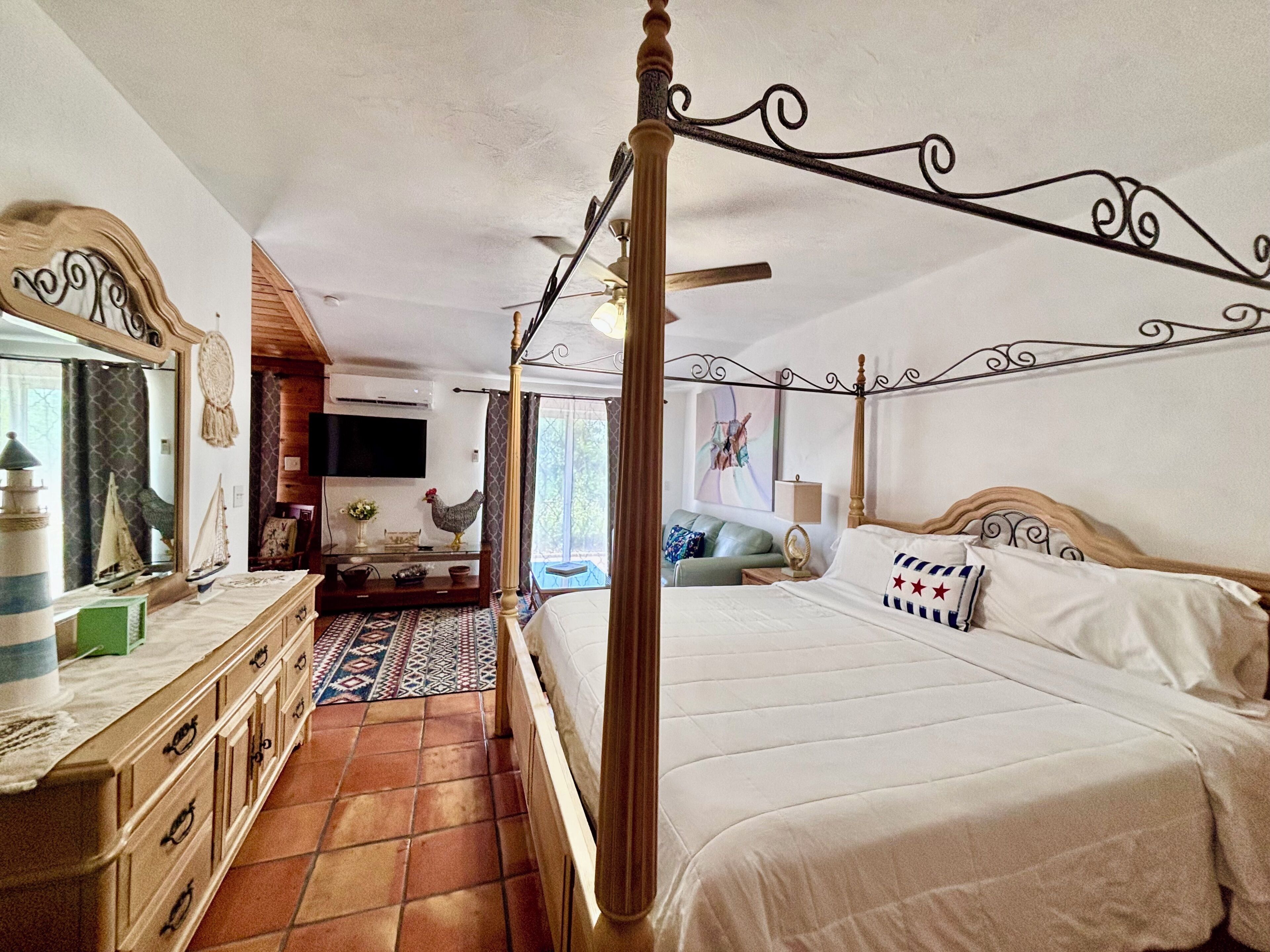 A four-poster bed with a wooden headboard, a television mounted on the wall, and a dining area with a table and chairs.