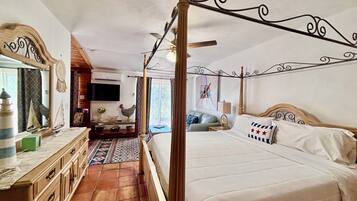 A four-poster bed with a wooden headboard, a television mounted on the wall, and a dining area with a table and chairs.