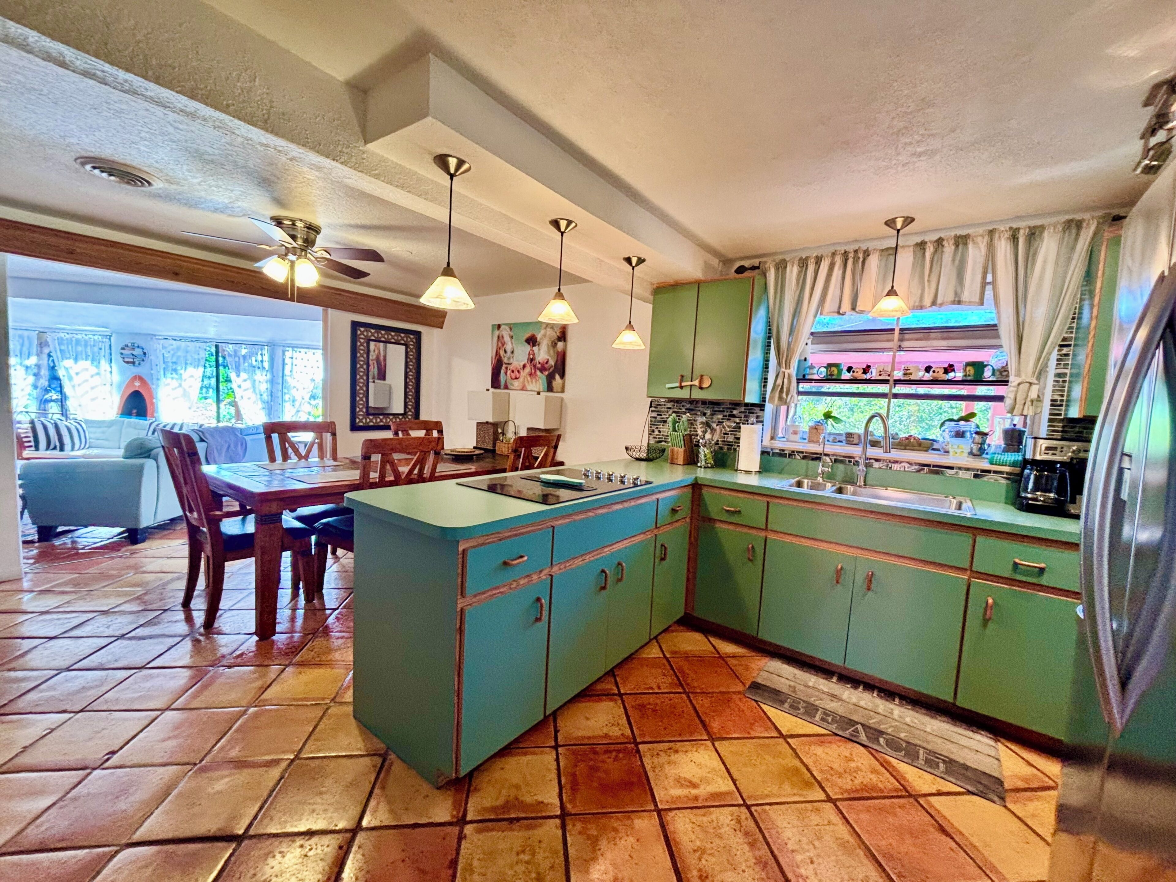 A kitchen with green cabinets, a tiled floor, and a dining area with chairs and a table.