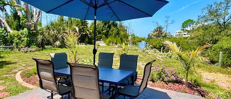 Eine Terrasse im Freien mit Tisch, Stühlen, einem großen Sonnenschirm und Blick auf einen See und viel Grün.