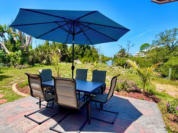 An outdoor patio with a table and chairs, a large umbrella, and a view of a lake and greenery.