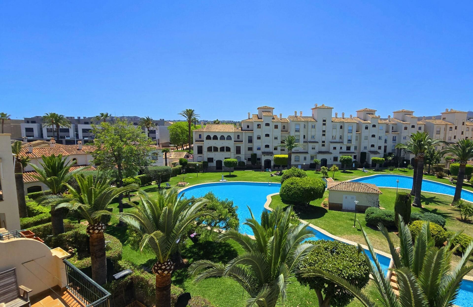 Een resort met meerdere zwembaden, weelderige begroeiing en een gebouwencomplex in mediterrane stijl.