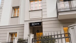 Un immeuble à plusieurs étages, sur lequel on peut lire l’inscription « BE MATE », doté d’une entrée sécurisée par un portail et d’un escalier menant à l’entrée.