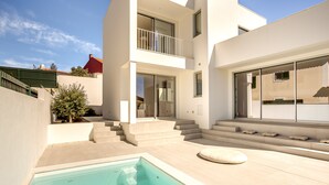 A modern residential building with a swimming pool, outdoor seating, and a staircase leading to a balcony. - Ericeira Modern Bright With Pool by Homing (Mafra)