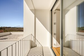 A modern balcony with a clear view of the landscape, a glass door leading to an interior space, and a white railing. - Ericeira Modern Bright With Pool by Homing (Mafra)