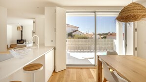 A modern kitchen with a large island, white cabinetry, and a view of a backyard through a sliding glass door. - Ericeira Modern Bright With Pool by Homing (Mafra)