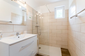 A modern bathroom with a sink, mirror, shower, and a small window.