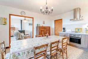 A dining area with a table set for four, wooden chairs, a chandelier, a kitchen with a stove and oven, and a wooden cabinet. - Gîte La Motette Drôme Provençale (Rousset les Vignes)