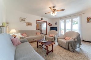 A living room with a sofa, armchairs, a coffee table, a ceiling fan, and a large window.
