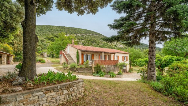 A house with a stone wall, a red-tiled roof, and a garden with various plants and trees. - Gîte La Motette Drôme Provençale (Rousset les Vignes)