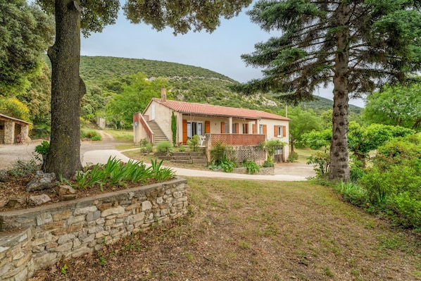 A house with a stone wall, a red-tiled roof, and a garden with various plants and trees.