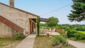 A building with a brick exterior, a covered patio with outdoor furniture, and a view of a lush green landscape. - Gîte La Motette Drôme Provençale (Rousset les Vignes)