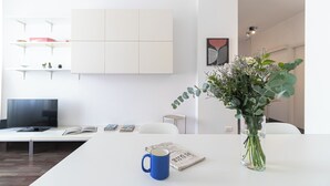 A modern living room with a white sofa, a coffee table with a blue mug and a newspaper, a TV, and a vase with green plants. - Italianway Easy - Papiniano 38 (Milan)