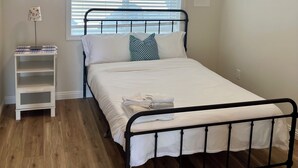 Un dormitorio con una cama individual, una mesita de noche, una ventana con persianas y un equipo de aire acondicionado.