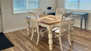 Un comedor con una mesa y sillas de madera, ventanas amplias con persianas y vistas al exterior.