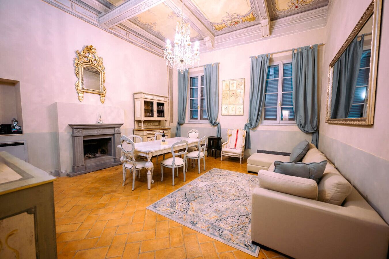 A spacious living room with a fireplace, a dining table with chairs, a sofa, and a chandelier.