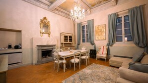 A spacious living room with a fireplace, a chandelier, a dining table with chairs, and a sofa. - Avignonesi - Tuscan Palace (Montepulciano)