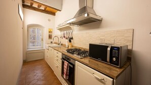 A compact kitchen with a gas stove, microwave, and stainless steel range hood. - Avignonesi - Tuscan Palace (Montepulciano)