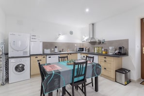 Una cocina moderna con electrodomésticos integrados, un comedor con mesa y sillas, y un cubo de basura pequeño.