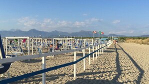 A beach with rows of sun loungers and umbrellas, a clear sky, and mountains in the background.