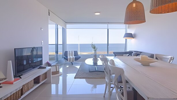 Een moderne woonkamer met een televisie, zitplaatsen, een eethoek en uitzicht op zee.