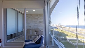 Een moderne kamer met een groot raam, een blauwe stoel en uitzicht op een weg en gebouwen.