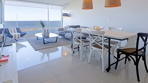 Een moderne woonkamer met een eetgedeelte, grote ramen en uitzicht op de oceaan.
