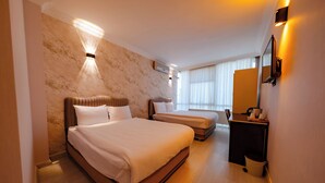 A hotel room with a large bed, a smaller bed, a desk with a chair, a mirror, and a window with blinds. - Koçaklar Otel (Karapınar)