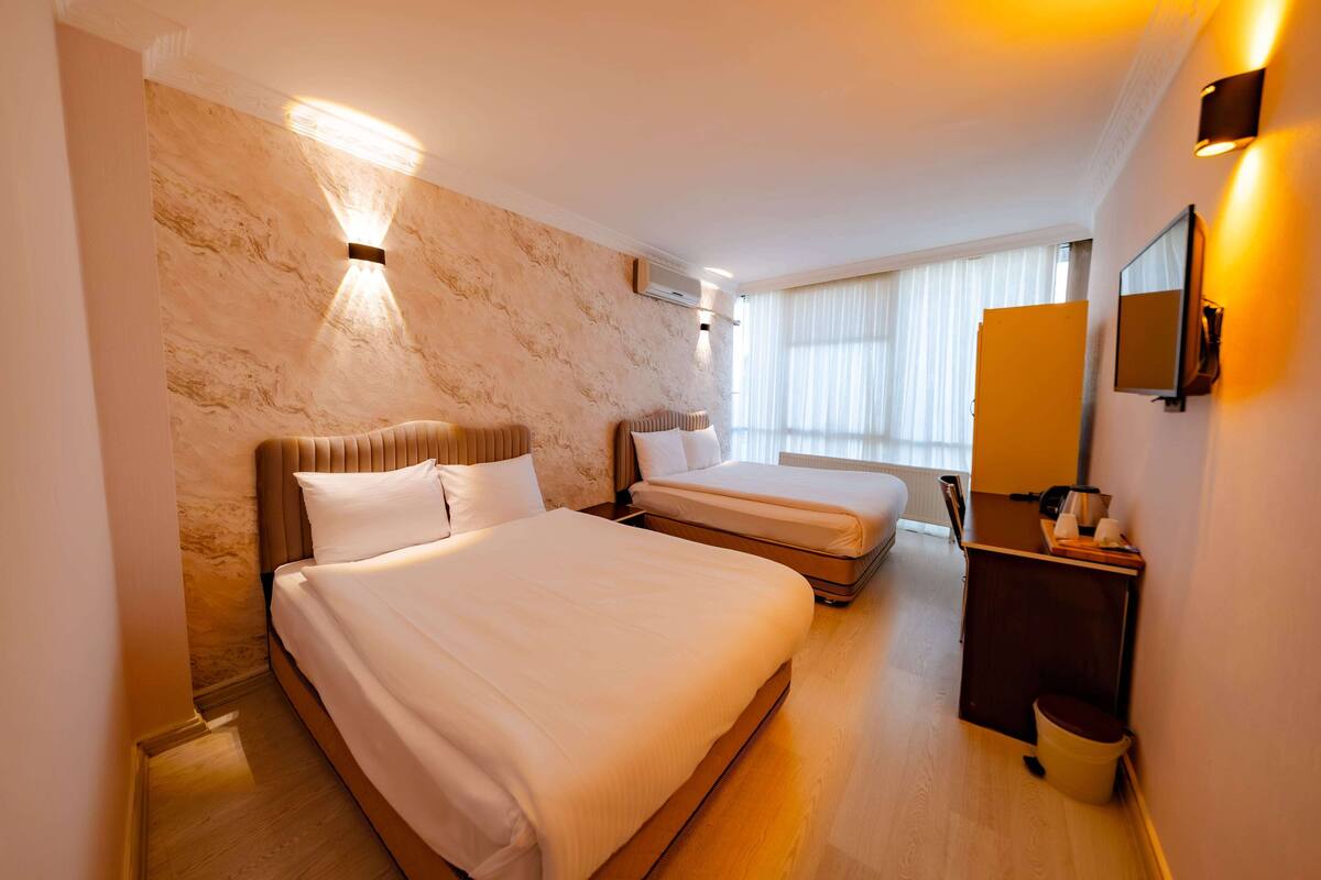A hotel room with two beds, a small desk, a mirror, and a window with curtains.