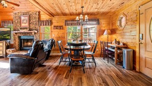 Ein gemütliches Blockhaus-Interieur mit Kamin aus Stein, Holzwänden, einem Essbereich und einer komfortablen Sitzecke.