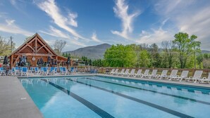 Ein Schwimmbecken mit Liegestühlen, ein Holzgebäude und eine Bergkulisse.