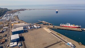 Vue aérienne d’un port où est amarré un grand navire de transport de marchandises, avec un quai et des bâtiments industriels.