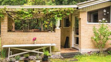 A brick house with a covered patio, a table, and potted plants.