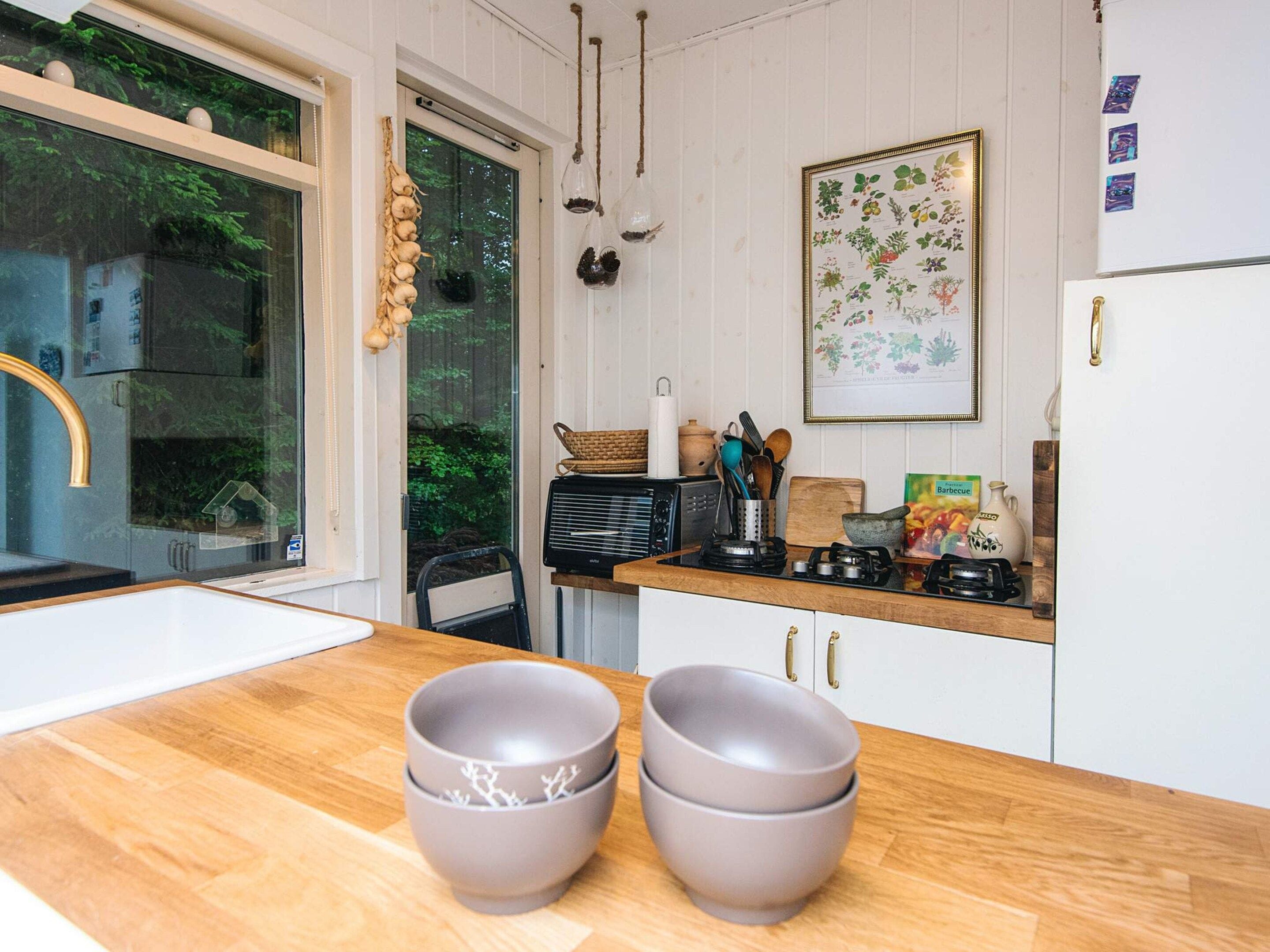 A kitchen with a wooden countertop, a sink, a refrigerator, and a window with a view of greenery.