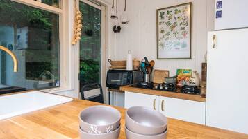 A kitchen with a wooden countertop, a sink, a refrigerator, and a window with a view of greenery.